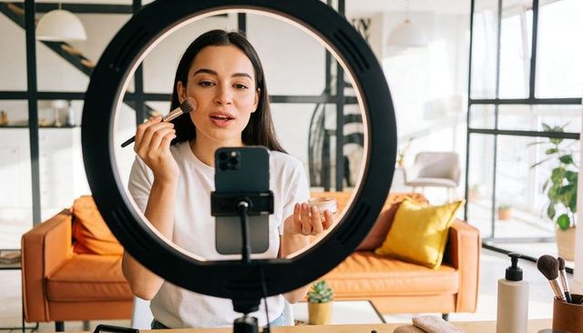 Beauty vlogger applying makeup on camera with ring light in bright home studio