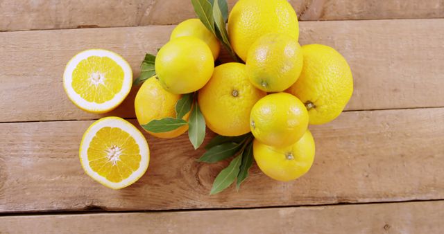 A bunch of fresh, ripe lemons with vibrant green leaves are displayed on a wooden surface, with one lemon cut in half to reveal the juicy inside. Lemons are often associated with health benefits, including high vitamin C content and potential detoxifying properties.