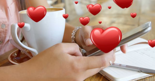 Close up of a pair of female hands texting beside a cup of coffee and a pen and notebook. Digital hearts are flying in the foreground 4k