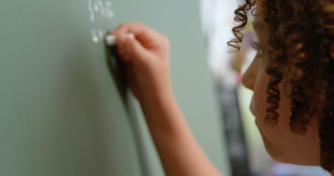 Boy with curly hair writing on chalkboard in school