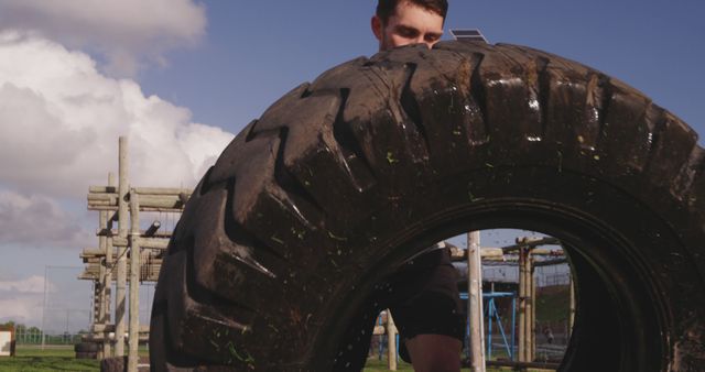 Male athlete engaged in tire flipping during outdoor training session. Suitable for fitness, exercise, and strength training-related content. Useful for promotional materials for gyms, personal training sessions, and health magazines capturing outdoor fitness activities.