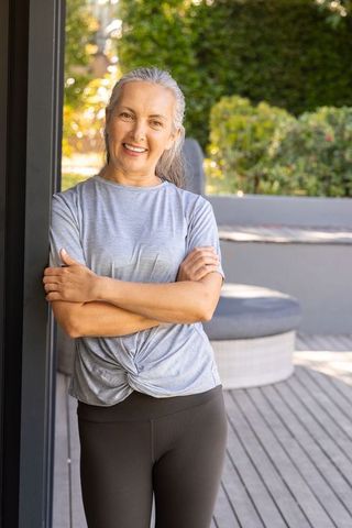 Smiling mature woman standing on sunlit patio wearing casual activewear