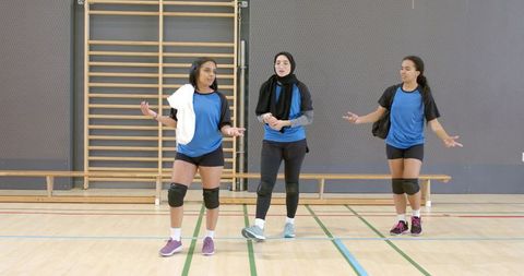 Diverse female volleyball teammates gesturing during indoor practice in blue jerseys