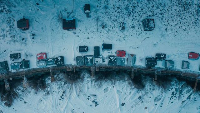 Drone aerial winter coastline with row cabins on frozen shore, wooden piers and red roofs