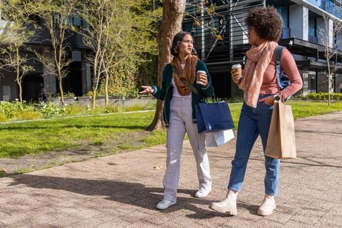 Diverse friends walking and shopping with coffee in sunlit urban park