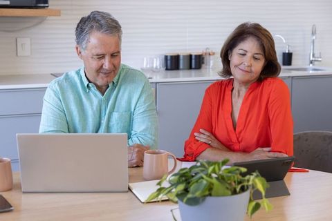 Mature couple working from home together in modern kitchen with laptop and tablet