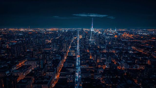 Neon avenue stretching toward illuminated spire over nighttime city skyline aerial view
