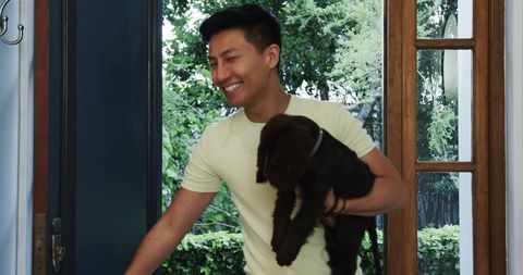 Man arriving home with adorable brown puppy in lush garden background