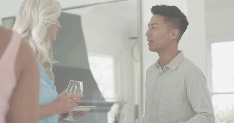 Asian man conversing with guest in modern kitchen during casual home entertaining with wine glass