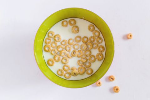 Top-down view of cereal rings floating in milk in green bowl on clean white background