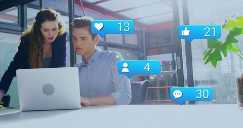Young professionals monitoring social media engagement on laptop in modern glass office