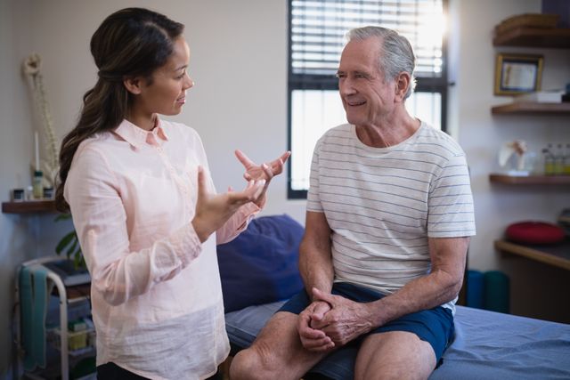 Senior patient sitting and consulting with a female therapist in a hospital ward. The therapist is gesturing while providing medical advice. This image can be used for healthcare, medical consultation, patient care, geriatric care, and wellness-related topics.