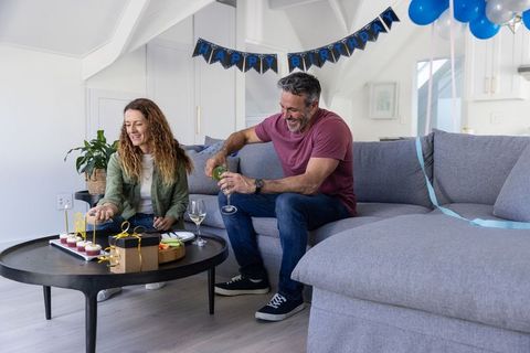 Couple celebrating birthday on gray sectional sofa with cupcakes balloons and wine