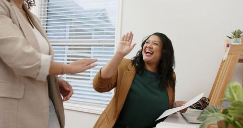 Female Coworkers Joyfully High-Fiving at Office Desk Celebrating Team Success and Collaboration