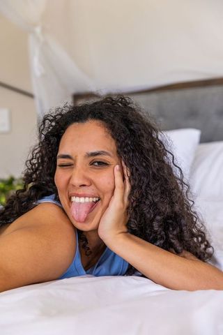 Playful african american woman winking and sticking out tongue while resting on bed