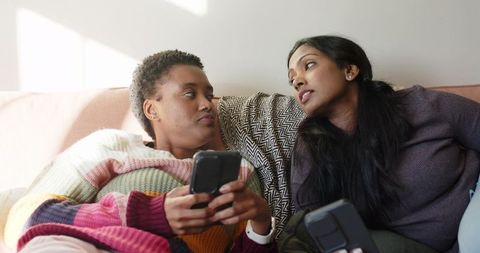 Diverse Friends Relaxing on Sofa Engaging with Smartphones at Home