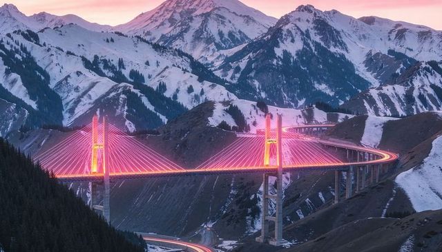Glowing neon cables illuminating cable-stayed viaduct curving through snow-capped mountain pass