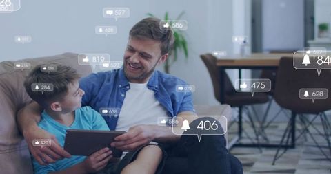 Smiling father and son sharing tablet on sofa with floating social media notifications
