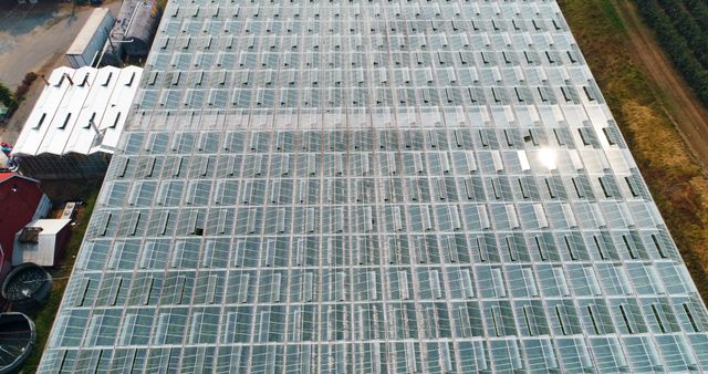 Aerial view of a large modern greenhouse showcasing the extensive network of glass panels. Useful for topics on industrial agriculture, sustainable farming, horticulture practices, greenhouse technologies, or commercial farming. Can be used in articles, farming industry presentations, and educational content on green technology and modern agriculture.