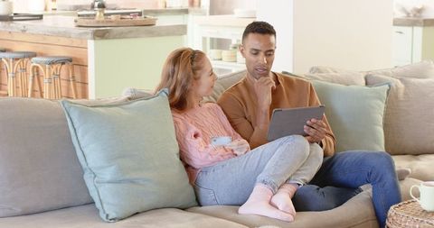 Diverse couple embracing technology together in cozy living room