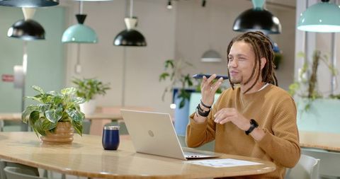 African American man speaking into smartphone while working on laptop in modern coworking space
