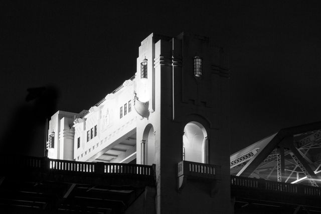 This bridge tower illuminated at night in black and white captures a dramatic urban architectural scene. The stark contrast of light and shadow emphasizes the intricate design and historic ambiance. Ideal for use in projects related to architecture, urban landscape, historic structures, and nighttime photography studies.