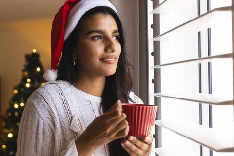 Woman in santa hat holding mug by window, warm holiday atmosphere