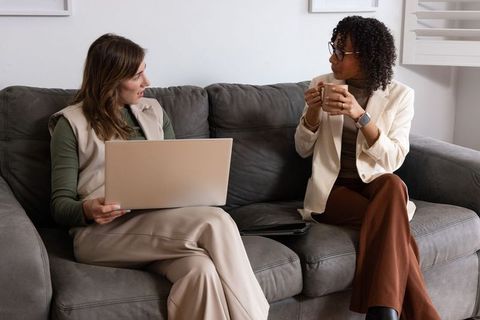 Diverse female colleagues collaborating on laptop and coffee during casual office meeting