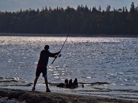 Fisherman on beach casting line into calm ocean