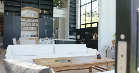 Sunlit minimal open-plan living room featuring white sofa, rustic wood coffee table, dark cabinets