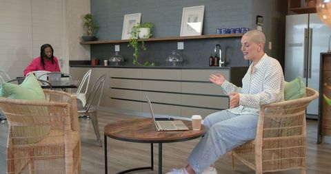 Woman video calling in modern coworking lounge with rattan chairs and casual collaboration