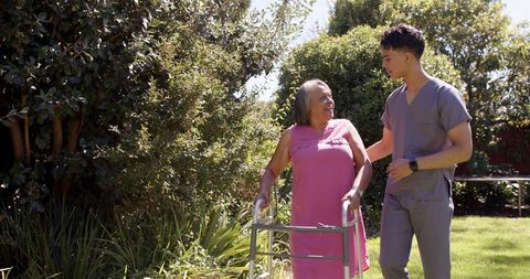 Smiling caregiver assisting senior woman with walker outdoors