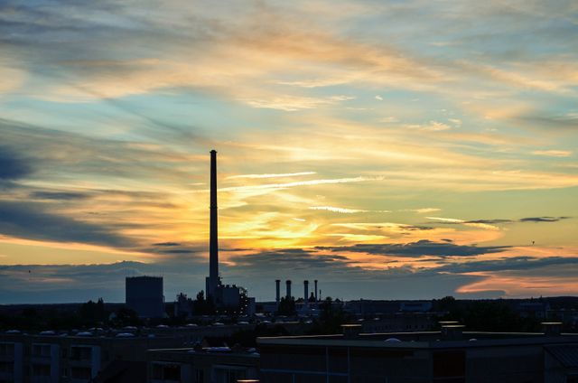 This image showcases an industrial facility with tall smokestacks silhouetted against a vibrant sunset sky. The wispy clouds add to the dramatic effect, creating a contrast between natural beauty and man-made structures. Use this image in environmental awareness campaigns, urban studies presentations, or to convey the juxtaposition of industry and nature.