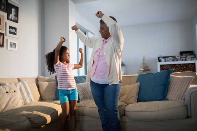 Grandmother and granddaughter dancing in living room at home