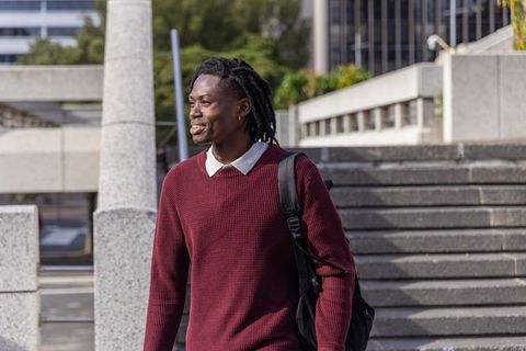 Young african american man walking urban steps wearing maroon knit sweater and backpack