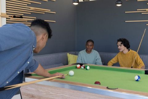 Young friends playing pool in modern lounge corner, casual indoor billiards hangout for groups