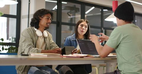 Diverse young professionals collaborating around laptop in modern coworking space