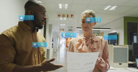 Colleagues collaborating over report in open-plan office with social media notifications