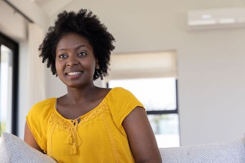 African american woman sitting, smiling on modern sofa in mustard blouse, portrait