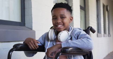 Smiling teen sitting in wheelchair wearing headphones on shaded campus walkway