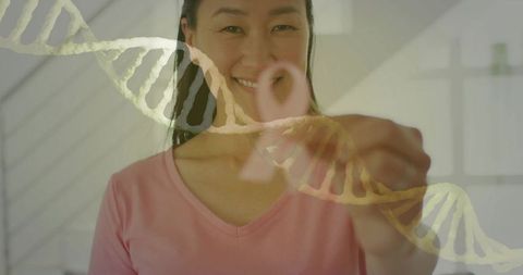 Asian woman drawing pink ribbon on glass with dna helix overlay for breast cancer awareness