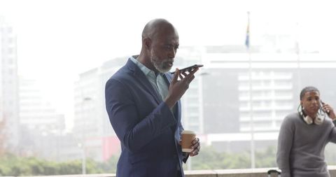 African american executive speaking into smartphone while holding coffee on urban terrace