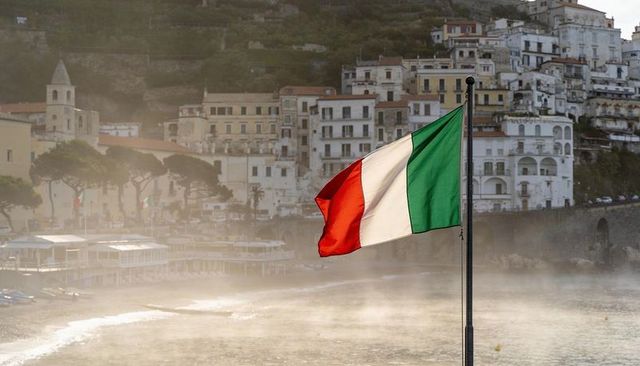 Italian flag fluttering over misty seaside town on amalfi coast catching warm sunlight