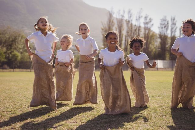Group of children participating in a sack race in a park on a sunny day. They are smiling and having fun, showcasing teamwork and energy. Ideal for use in educational materials, advertisements for outdoor activities, or promoting children's events.