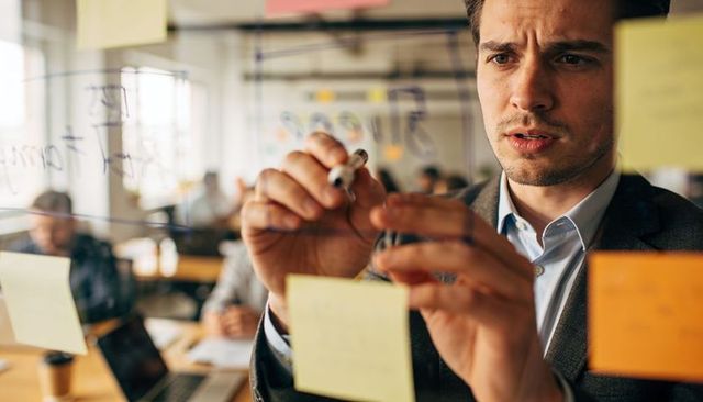 Focused businessman planning strategy on glass wall with sticky notes and marker