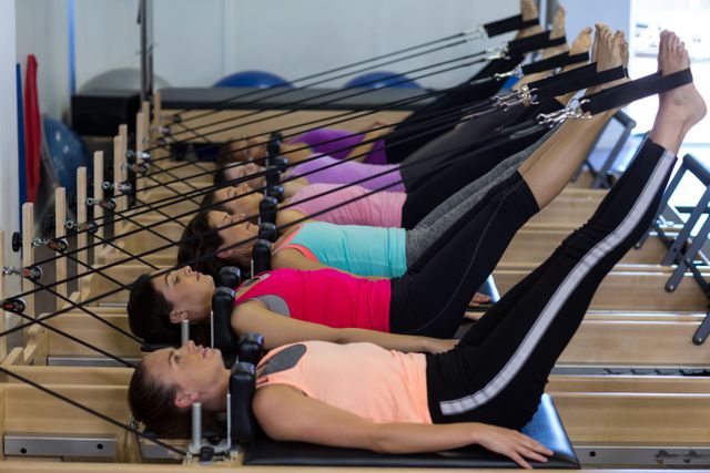 Women are depicted doing Pilates exercises on reformer machines in a gym. This can be used to illustrate fitness routines, gym activities, or healthy lifestyles. Ideal for promoting fitness classes, gym memberships, and health and wellness blogs.