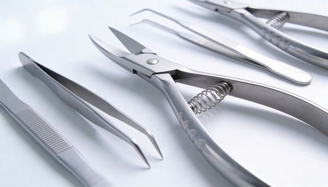 Precision steel nipper with coil spring and straight bent tweezers on white tray closeup