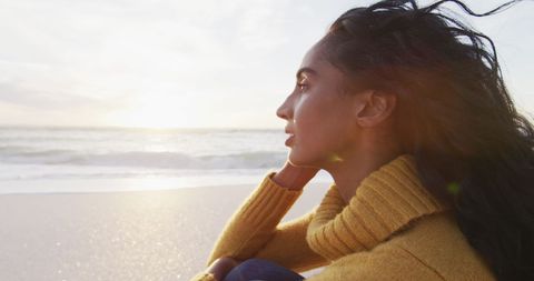 Thoughtful Woman in Cozy Sweater Enjoying Beach Sunset