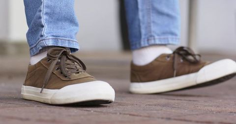 Brown canvas sneakers walking on wooden deck with light blue jeans and white ankle socks