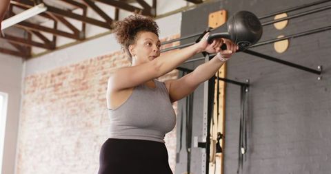 Woman performing kettlebell swing in industrial gym building strength and endurance